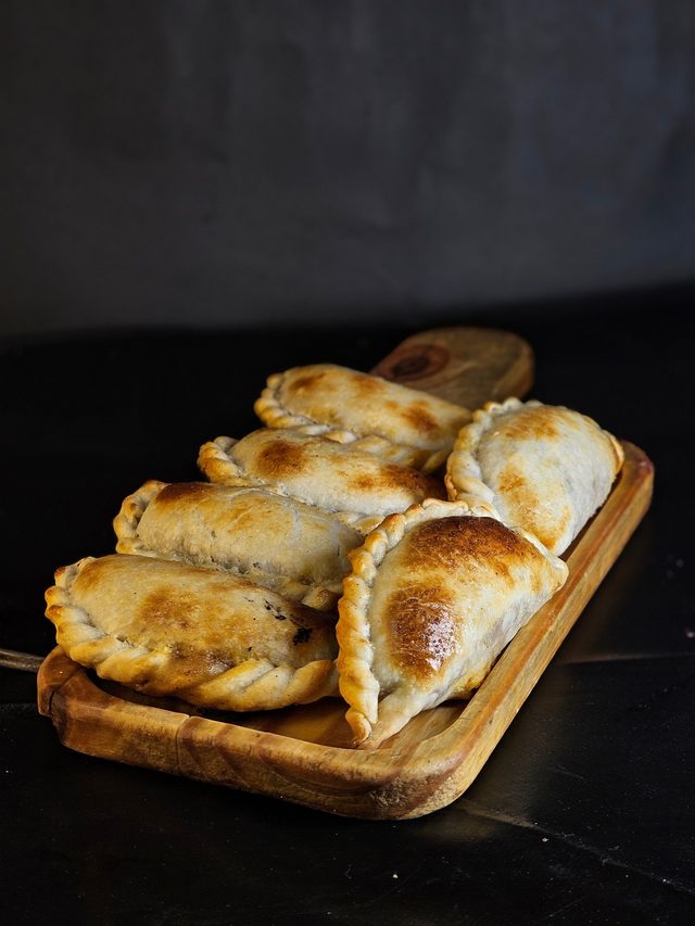 Empanadas doradas sobre tabla, fondo oscuro